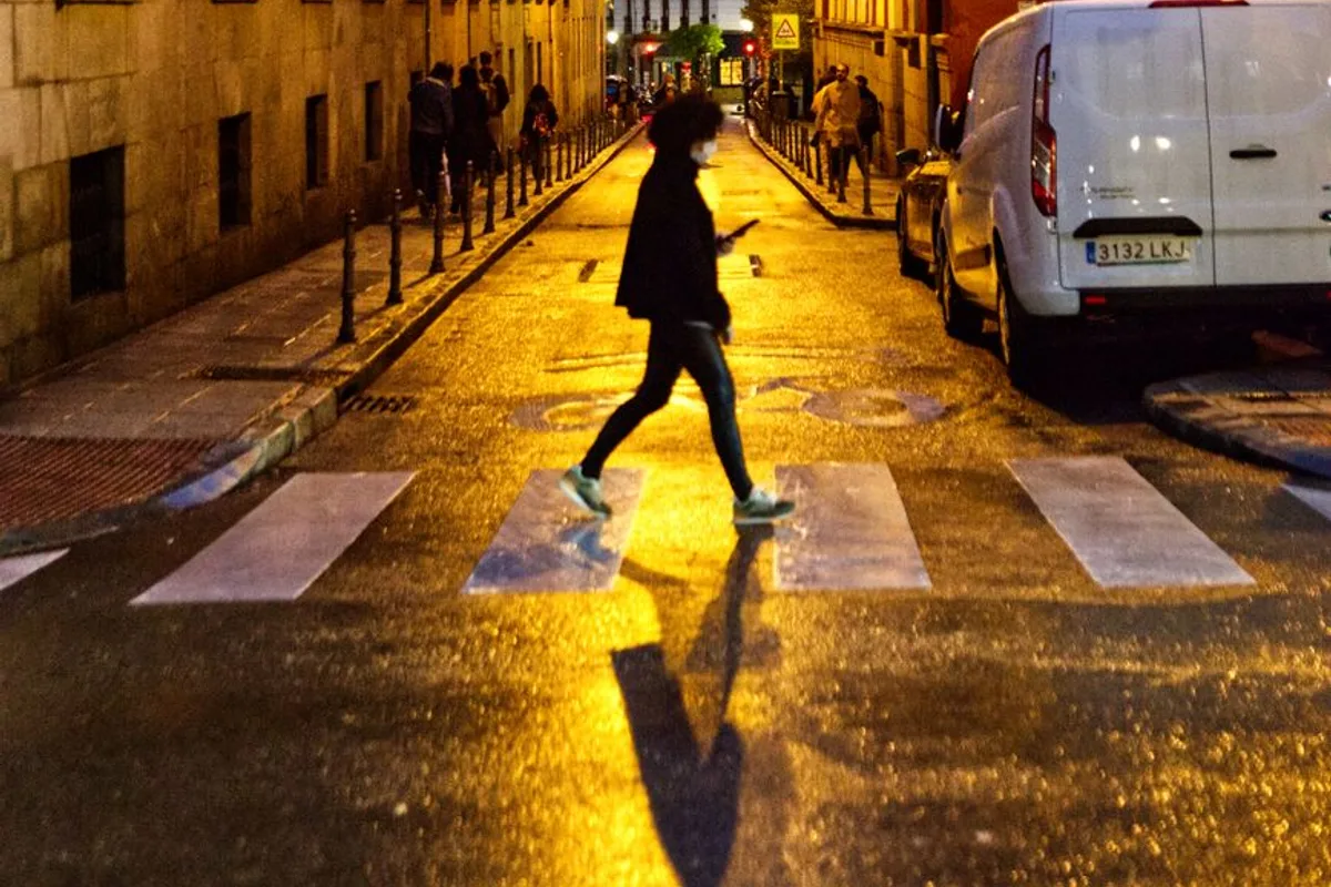 A pedestrian crosses a rain-slicked Madrid street lit by golden streetlight at night