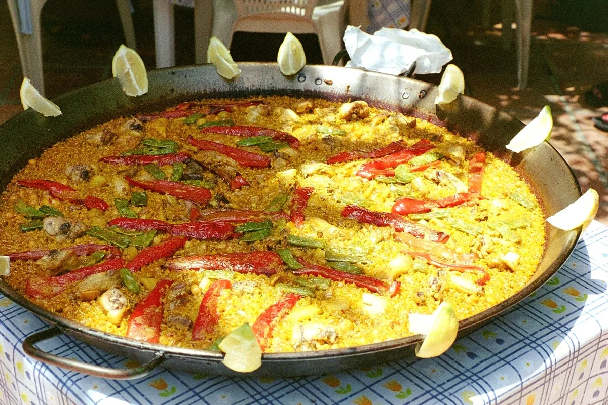A large pan of freshly cooked Spanish paella garnished with lemon wedges